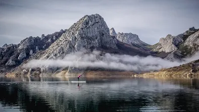 Ein Mädchen oder eine Frau mit rosa Mantel übt Paddelsurfen in einem Bergsee mit Nebel