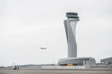La tour de contrôle moderne de l'aéroport d'Istanbul, avec un avion au décollage et un hélicoptère stationné au premier plan.