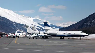 Avions privés stationnés à l'aéroport de St Moritz, entourés de montagnes enneigées.
