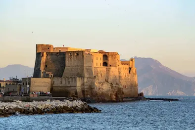 Paesaggio del golfo di Napoli in Italia con un castello medievale in primo piano, un punto di riferimento della città, di fronte alle montagne in lontananza, una bella giornata con tempo perfetto all'ora del tramonto