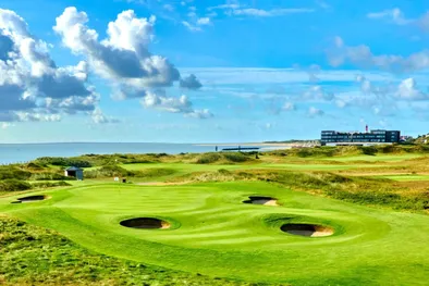 Campo da golf verde con bunker rotondi con un hotel e il mare sullo sfondo