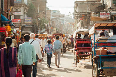 A bustling street scene in Delhi, India, showcasing the vibrant daily life with people walking and rickshaws navigating the crowded road.