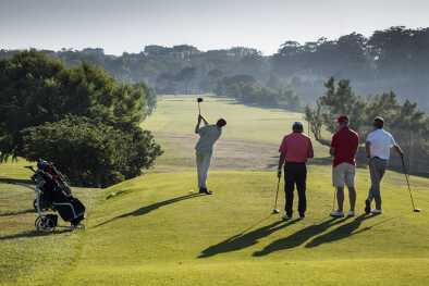 A group of golfers watch a golfer tee off in the sunshine